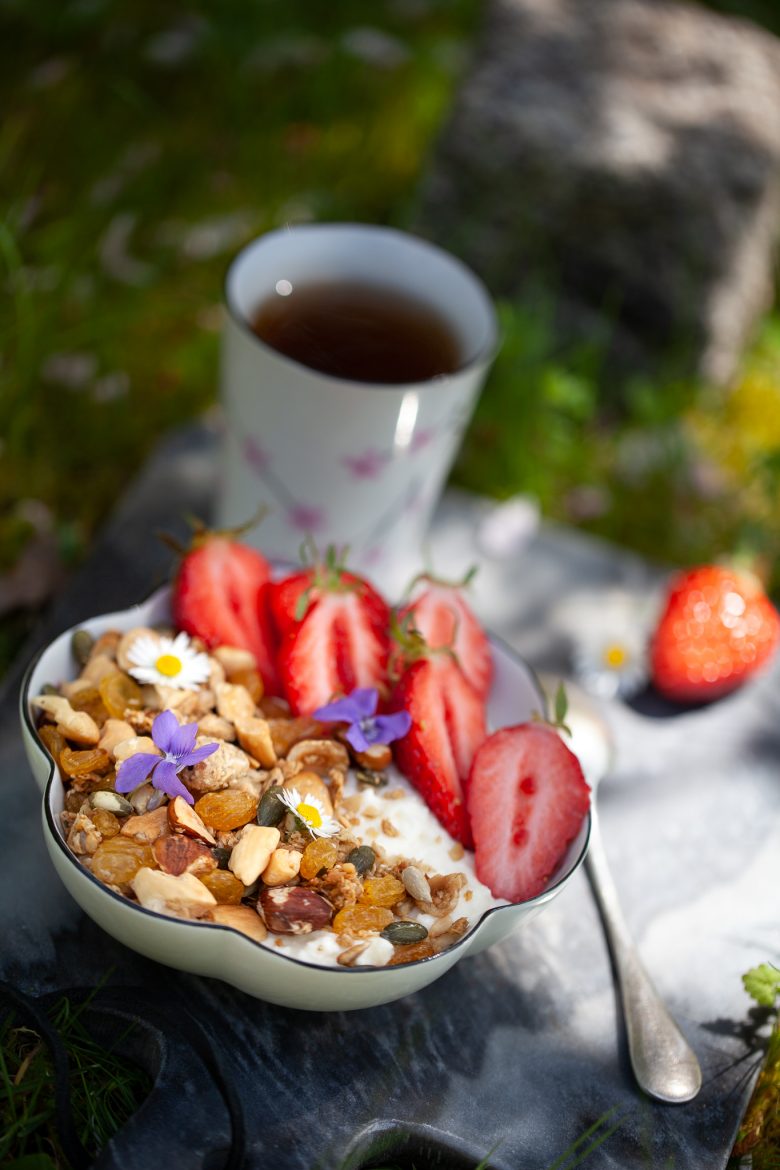 Pique Nique petit déjeuner composé de brousse de brebis, de granola, de fraises et de fleurs de jardin