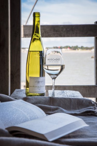 Bouteille de vin blanc de Gros-Plant et verre de vin, devant l'océan et livre ouvert