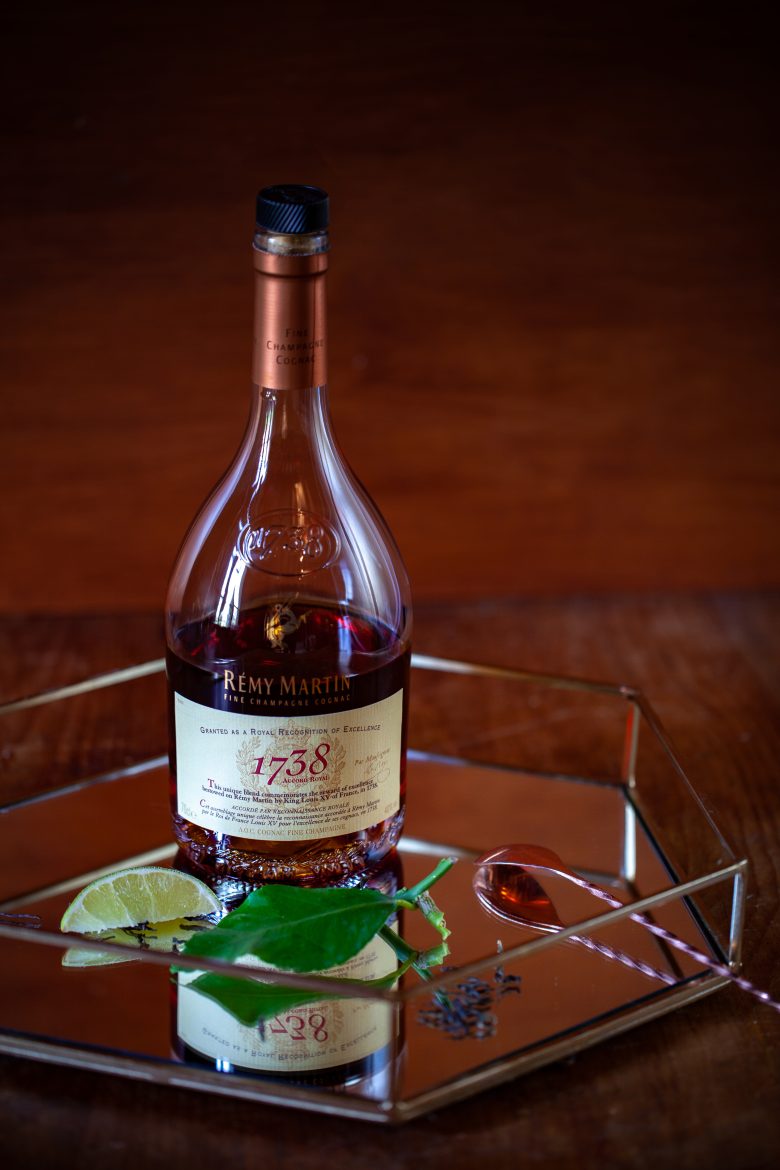 Bouteille de cognac Fine Champagne Remy Martin 1738 accord royal sur un plateau en verre, feuille et tranche de bergamote